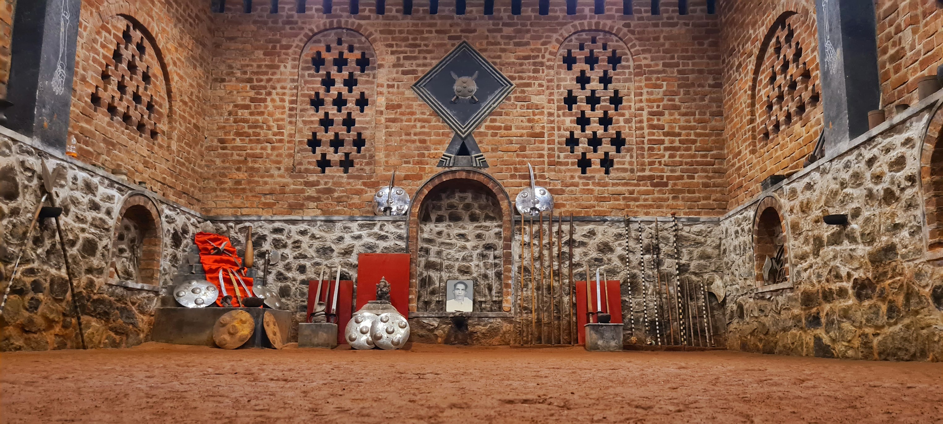 Traditional Buddha Kalari Academy training hall with authentic brick architecture and complete display of Kerala martial arts weapons and shields