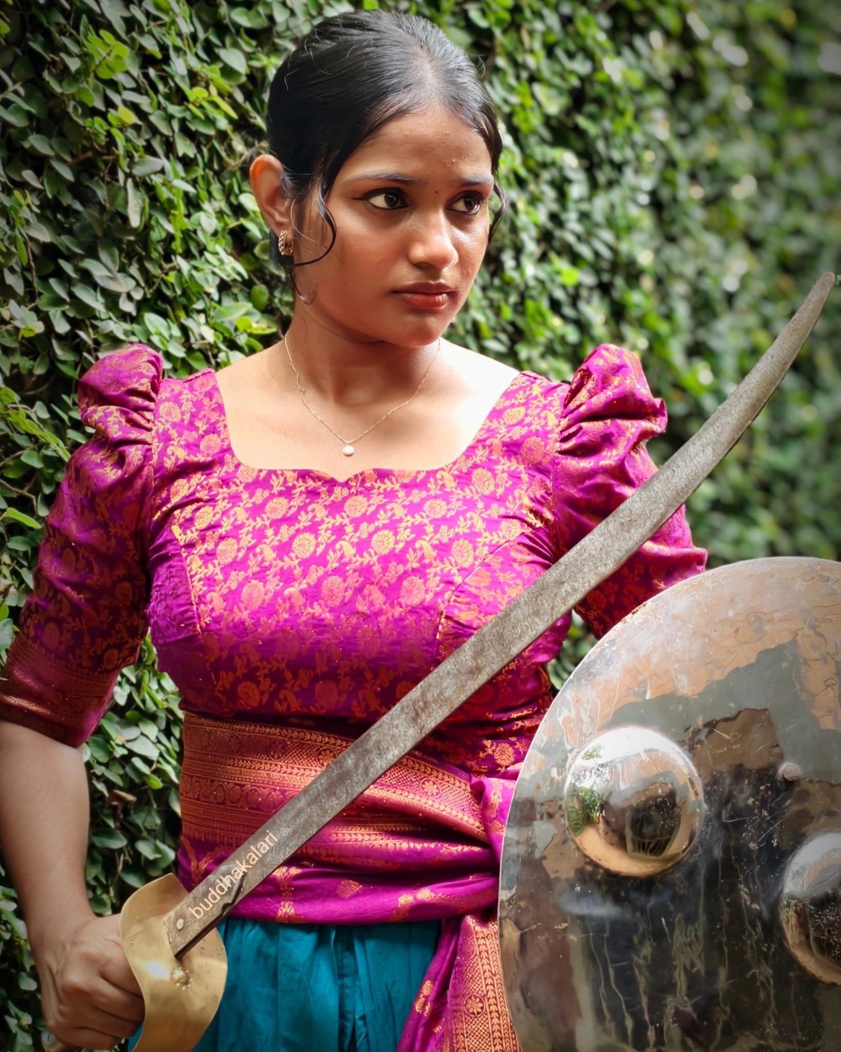 Female Kalaripayattu practitioner in traditional Kerala costume demonstrating sword and shield techniques in authentic training attire