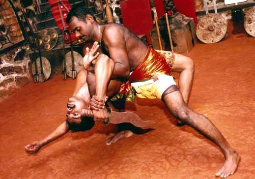 Kalaripayattu ground combat training with practitioners in traditional red and gold attire demonstrating close-quarters fighting techniques