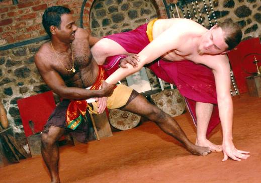 Traditional Kalaripayattu combat stances with practitioners in authentic red and gold Kerala martial arts attire demonstrating fighting positions